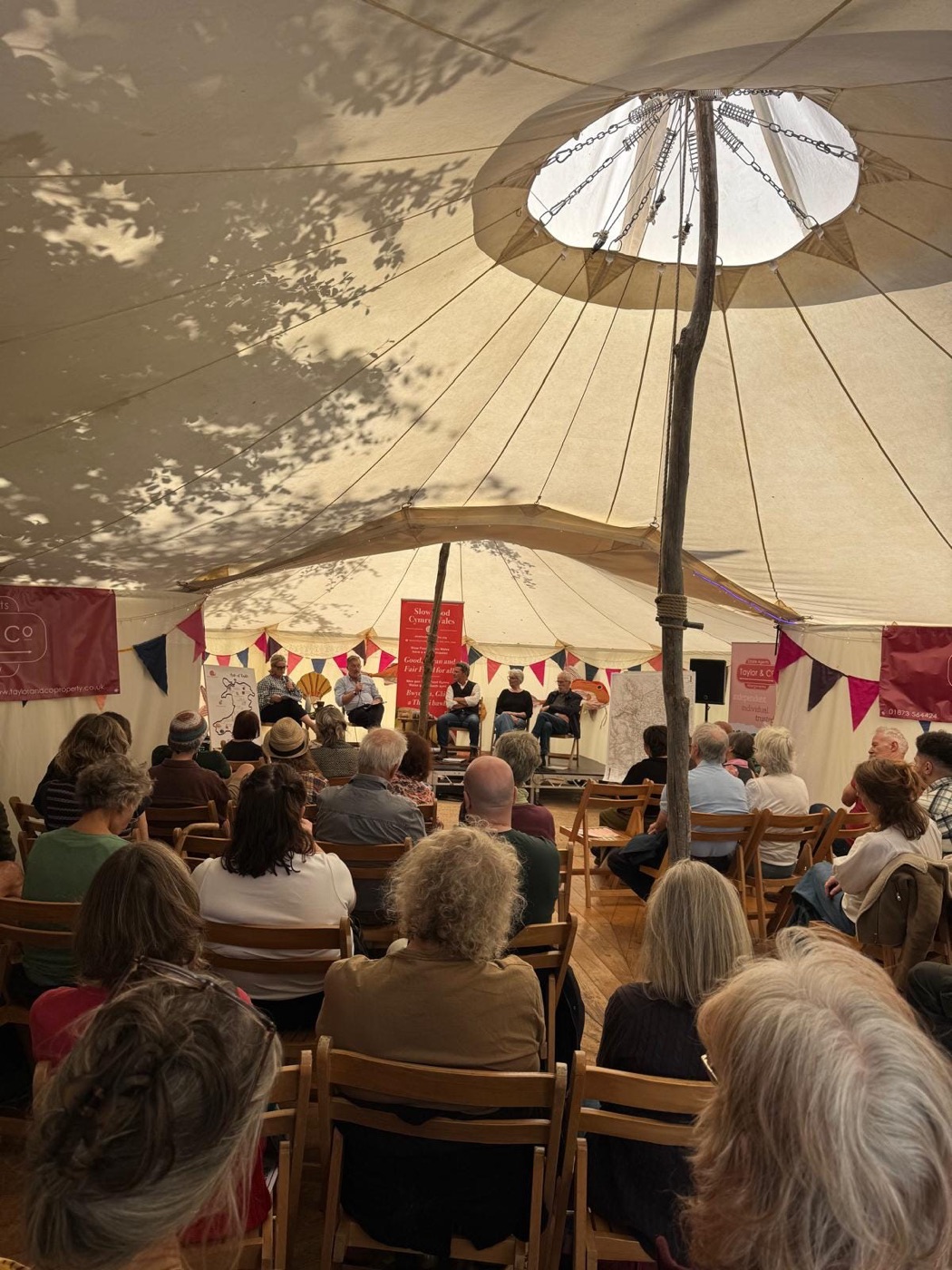 A seated audience filling a bell tent, seen from the back