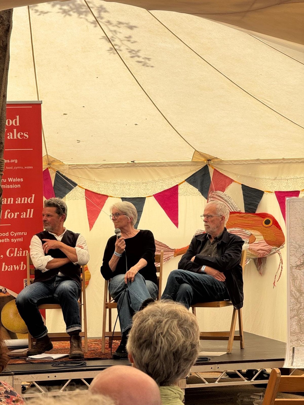 Three speakers in conversation on stage beside a Slow Food Cymru Wales banner