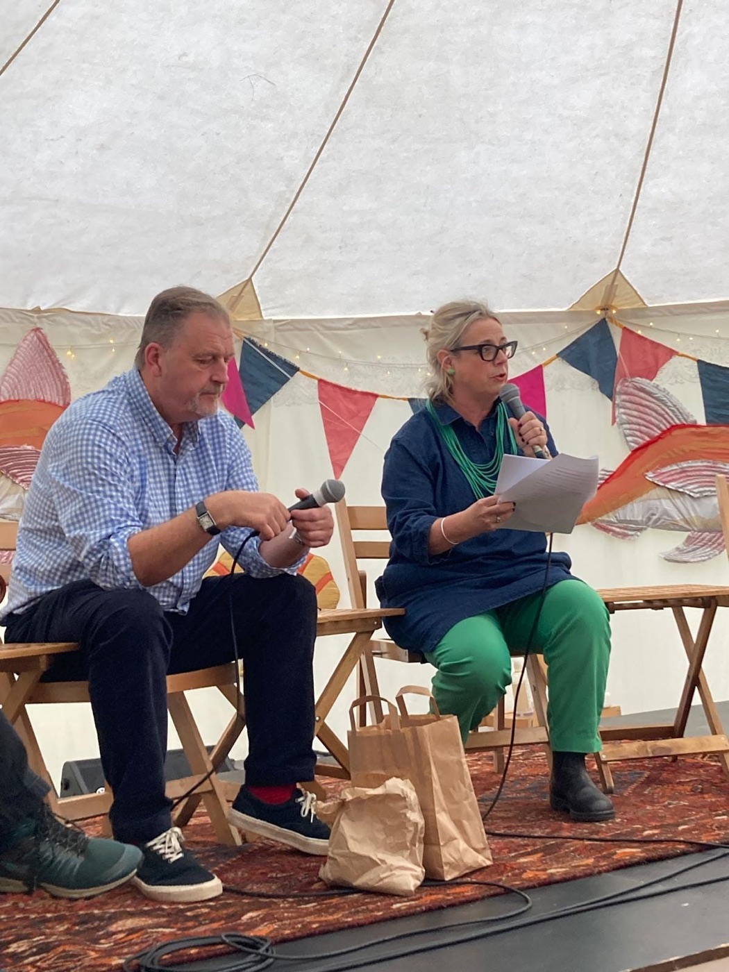 Two Slow Food Cymru Wales speakers with microphones on a stage under a bell tent strung with bunting