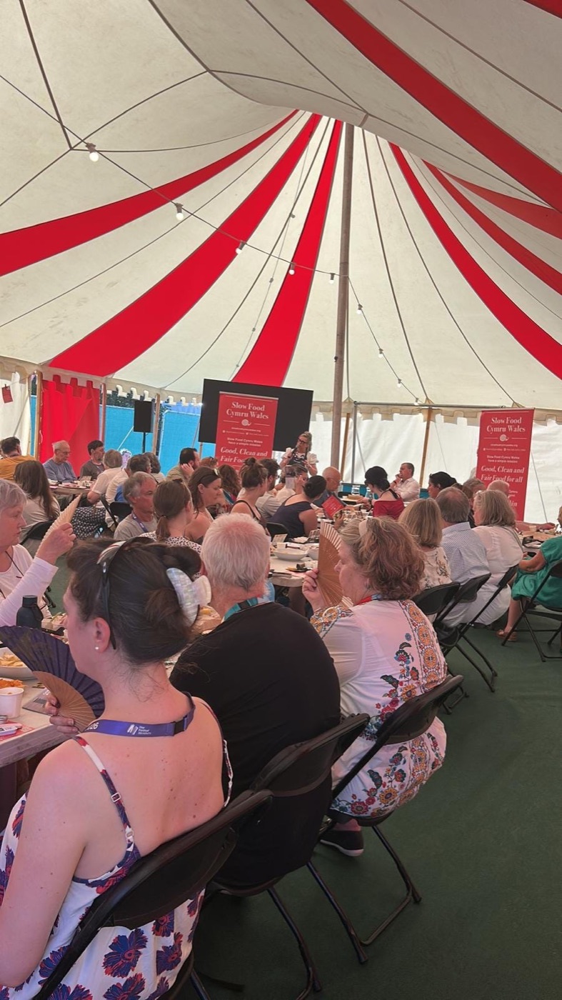 A packed red-and-white striped festival tent with Slow Food Cymru Wales banners at the front
